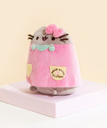 Quarter view of the front of the Pusheen Plush, showing the Hello Kitty x Pusheen collaboration logo on the pocket. The dress goes down to Pusheen's feet, leaving her bottom exposed.