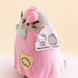 Side view of the plush, showing the product tag for the item. The tag features artwork of Hello Kitty sitting across from Pusheen, who is wearing Hello Kitty's bow. A rainbow with Hello Kitty's bow connects the two.