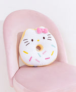 Hello Kitty side of Donut Plush sits on a pink desk chair to demonstrate the scale of the plush. Hello Kitty has brown eyes and whiskers to accompany her classic yellow nose.  