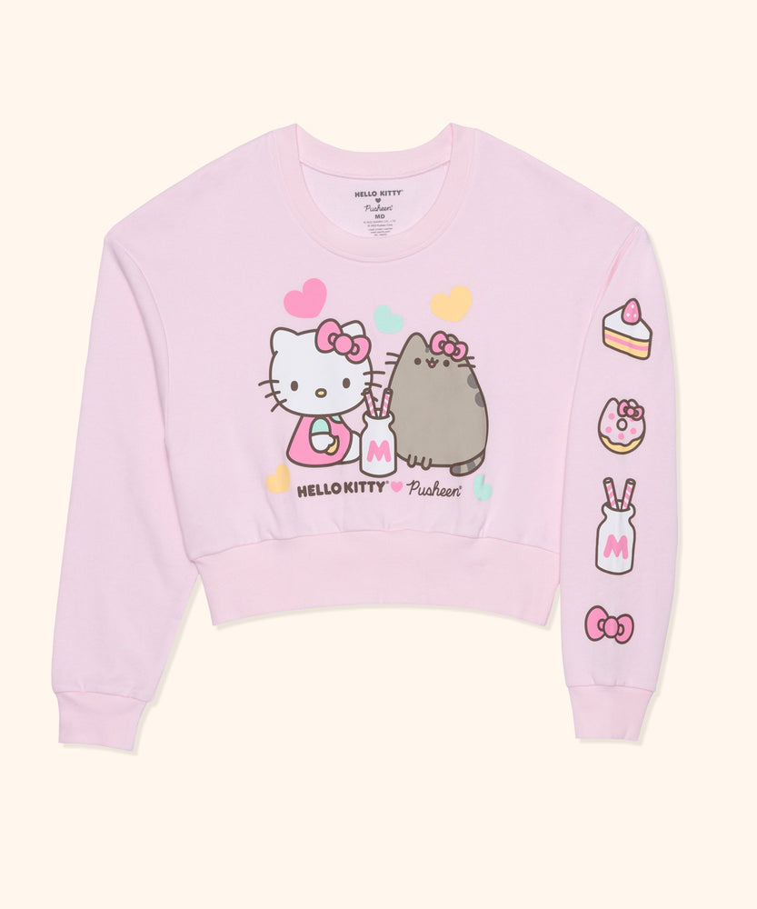 Front view of ladies cropped sweatshirt with the left sleeve folded to reveal the sleeve design that starts at the shoulder and finishes at the shoulder cuff.  up of the right side of the tee. A slice of cake, a donut, a milk bottle, and Hello Kitty's bow is are screen printed onto the light pink sweatshirt.