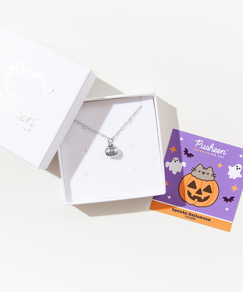 The silver charm necklace in a square white jewelry box. A square card insert is next to the box, featuring artwork of the charm.