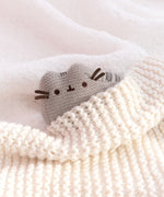 Mini Plush lies on a white, fluffy surface with a cream knit blanket covering half of the plush. The crocheted plush is snuggled into the blanket. 