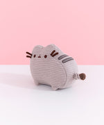 Left quarter view of mini knit Pusheen plush. This angle shows off the cat’s grey embroidered back stripes and knit, striped tail. 