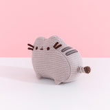 Left quarter view of mini knit Pusheen plush. This angle shows off the cat’s grey embroidered back stripes and knit, striped tail. 
