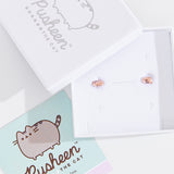 Rose gold vermeil finish of Pusheen Lazy Stud Earrings in their packaging. The earrings are placed inside a white box with a silver Pusheen the Cat logo next to a mint green informational card.  