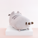 Back quarter view of the Medium Log Squisheen, facing the left, placed on top a square white pedestal in front of a light pink and white background. Pusheen’s behind is just as round as her front. Her striped tail sits directly in the middle of the circle. There are two nub feet at the bottom of the circle, mirroring the ones up front. 