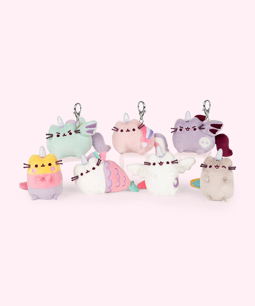 A small stacked line up showing the potential plush keychain designs in the set. The designs include Sunset Pusheenicorn, Dragon Pusheenicorn, Mermaid Pusheeinicorn, Fashion Pusheenicorn, Super Pusheenicorn, Spooky Pusheenicorn, and classic Pusheenicorn winking. 