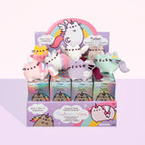 All of the Magical Pusheenicorn Surprise Plush resting on top of a cardboard display case holding the surprise box. The individual surprise boxes are iridescent, with an illustration of a classic Pusheenicorn winking. The box display is purple, featuring rainbows, clouds, and illustrations of various Pusheenicorns. The top of the display features Super Pusheenicorn standing proudly underneath a rainbow, her respective surprise plush underneath her.