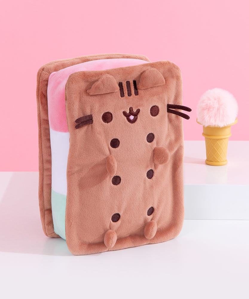 Front and side view of the Neapolitan Ice Cream Sandwich Pusheen Squisheen Plush. Pusheen takes the form of a tri-colored ice cream dessert. The rectangle shaped plush has brown “sandwich” pieces with dark brown circles to indicate holes. Pusheen’s face is is embroidered in a matching dark brown thread color. 