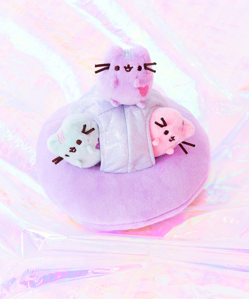 The Mini Pastel Pusheen riding their space ship across the holographic sea. The Mint and Pink Pusheen poke their heads out from the windows, while the lilac Pusheen sits on top of the ship. 