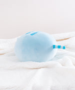 The back quarter view of the Blue Round Squisheen Plush sitting on top a fluffy white blanket. All the stripes on Blue Pusheen are a Dark Blue.