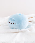 The Blue Round Squisheen Plush sitting alone in a quarter profile in a sea of a fluffy white blanket, a singular, perfect blue orb.