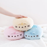 A trio of Round Squisheen plush stacked up in the shape of a triangle, pink and blue at the bottom with the yellow on top. A model’s hand is resting on top of the triangle.