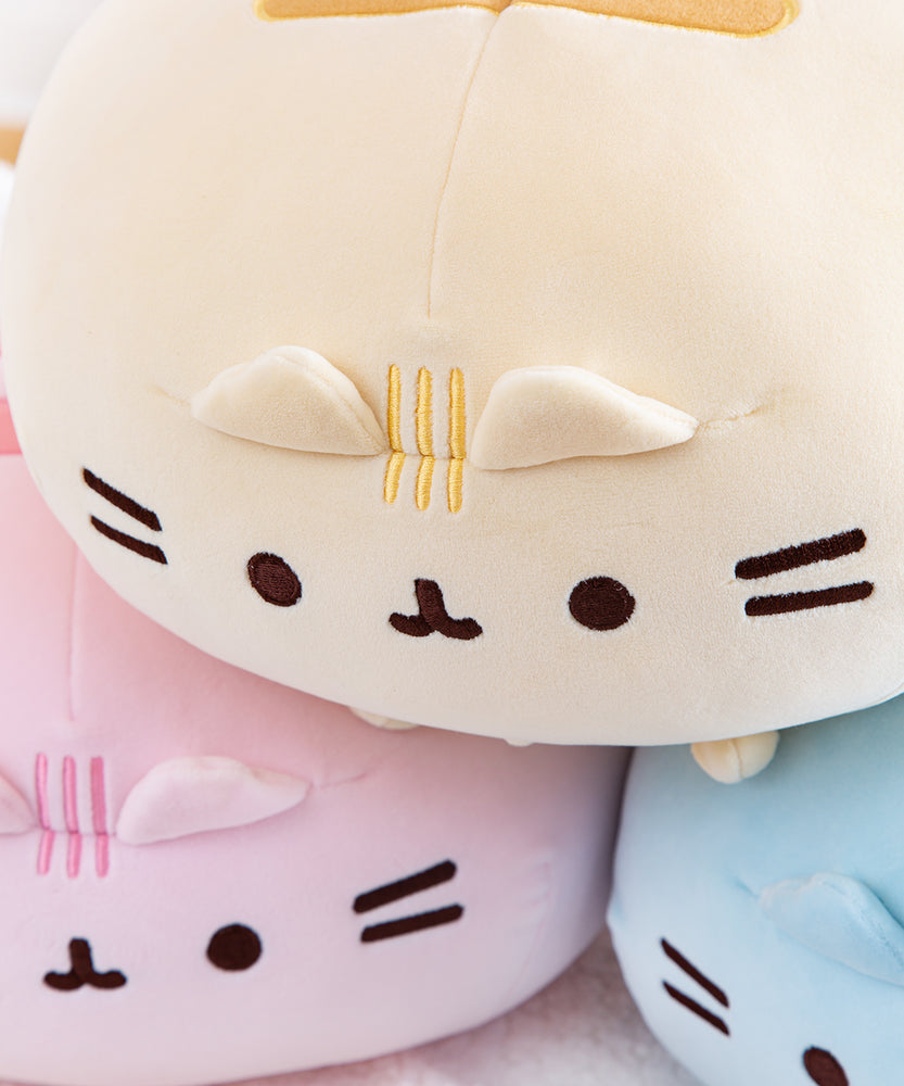 Close up of the Round Squisheen plush stacked up in the shape of a triangle, pink and blue at the bottom with the yellow on top. The round squisheen’s ears poke out from a seam, which the head stripe embroidery goes through. Pusheen’s eyes, mouth and whiskers are embroidered in dark brown thread.