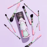 Brush set and storage tube lay in on a purple background. The storage tube features a graphic of pink, mint, and purple Pastel Pusheens with a UFO above the cats.  