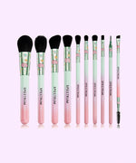 10-piece Brush Set stands in front of a purple background. The handle of the makeup brushes starts off pink at the bottom and transitions to purple and then to a mint green close to the barrel. Synthetic brush hairs are black. 