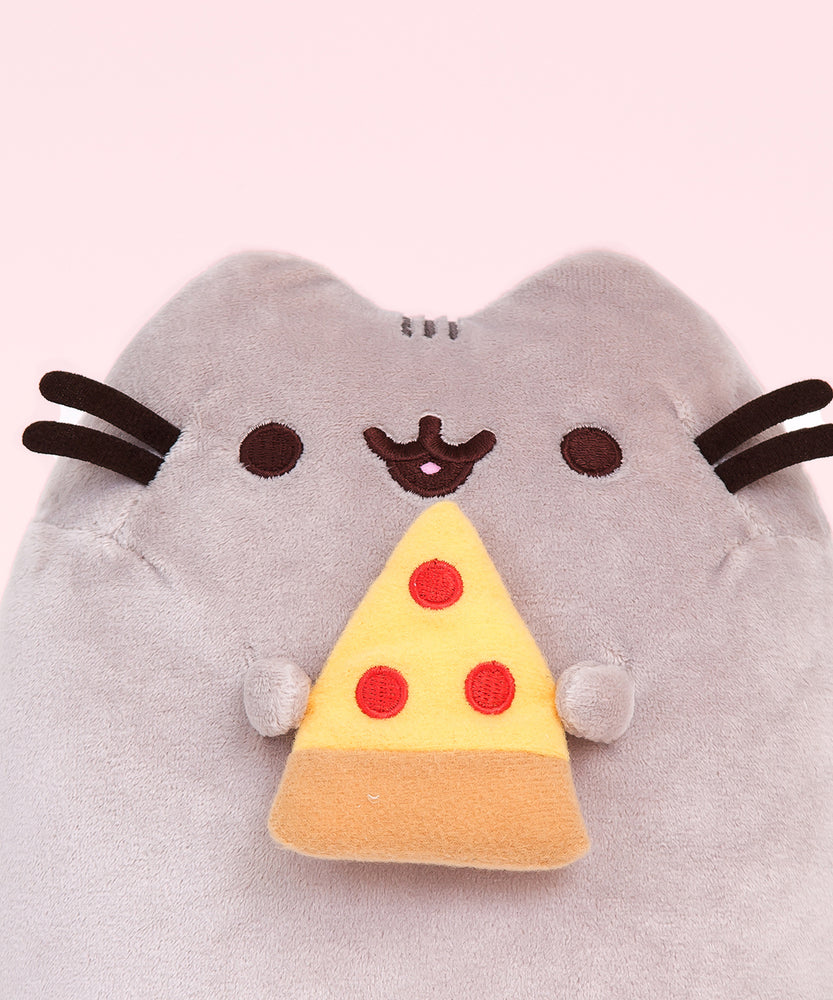 Closeup view of Pizza Pusheen Plush. In her paws, Pusheen holds a yellow, red, and light brown slice of pizza representing pepperoni pizza. She is shown with her classic black and brown nose, eyes, and whiskers.