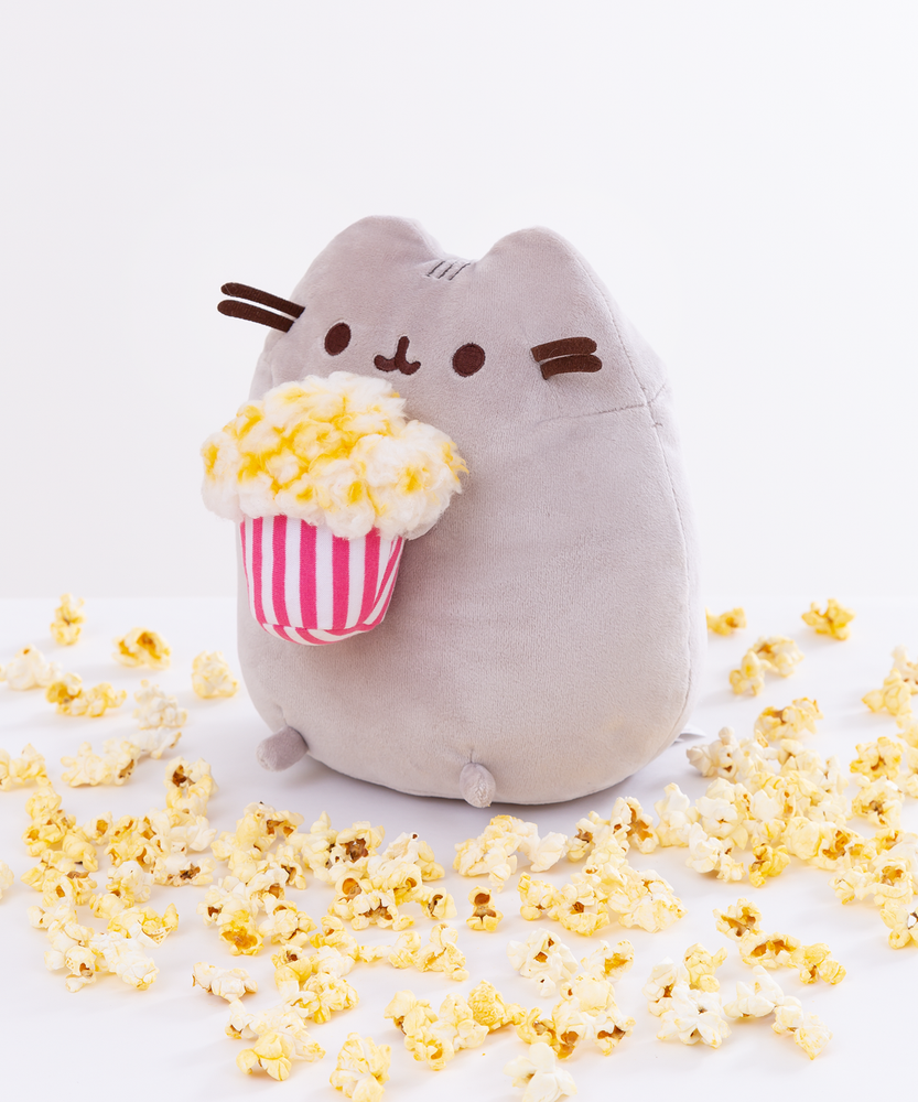 Quarter view of the Popcorn Pusheen Plush facing the right in front of a white background, loose popcorn pieces surrounding the ground around her.