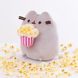 Quarter view of the Popcorn Pusheen Plush facing the right in front of a white background, loose popcorn pieces surrounding the ground around her.