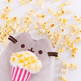 The Popcorn Pusheen Plush peeking out from the lower left corner, loose popcorn pieces strewn all above her. 
