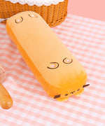 Bottom view of the baguette plush. The black and pink embroidery mimics a cat’s paw pad. The surface of the plush is a mix of gold and cream. 
