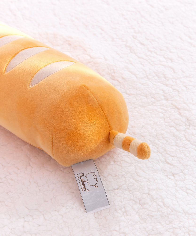 Back view of the baguette bread squisheen. The elongated plush has light cream wavy stripes on the top of the plush. At the back bottom of the plush is a light brown and cream striped tail. 