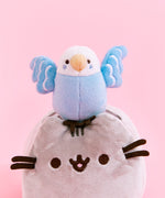 Back quarter view of the Bo and Pusheen Plush. From this angle, Bo's tail reaches out to Pusheen's first back stripe. The back of Bo's wings do not have any white feathers embroidered in. Pusheen's tail is present on the other side of the log.