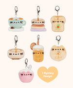 Front view of Pusheen Breakfast Surprise Plush assortment. Pusheen the Cat has taken the form of seven miniature breakfast-inspired plush varieties. From left to right and top to bottom, the surprise plush are a Latte, Pancake Stack, Avocado Toast, Waffle, Orange Juice, Sesame Bagel, and Bowl of CerealThe bottom right corner has a heart with the words “1 Mystery Design!” indicating eight possible miniature plush keychains are available.