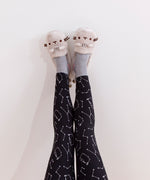 A pair of feet raised into the air, feet slightly angled by the heel, modeling the Pusheen plush slippers in front of a white background.. The tail on the plush slippers are slightly visible from this angle.