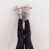 A pair of feet raised into the air, feet slightly angled by the heel, modeling the Pusheen plush slippers in front of a white background.. The tail on the plush slippers are slightly visible from this angle.