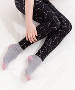Model sitting while wearing the Pusheen Celestial Leggings on top of a white fluffy blanket with a hand over the left leg. The leggings go down to the ankle.