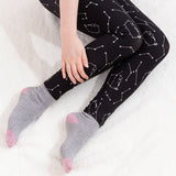 Model sitting while wearing the Pusheen Celestial Leggings on top of a white fluffy blanket with a hand over the left leg. The leggings go down to the ankle.