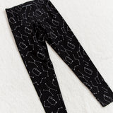 Top view of the Celestial leggings, laying flat at an angle on top of a fuzzy white blanket. The pattern on the leggings continues up to the elastic waistband. Some of the constellations in the legging pattern includes the Big Dipper.