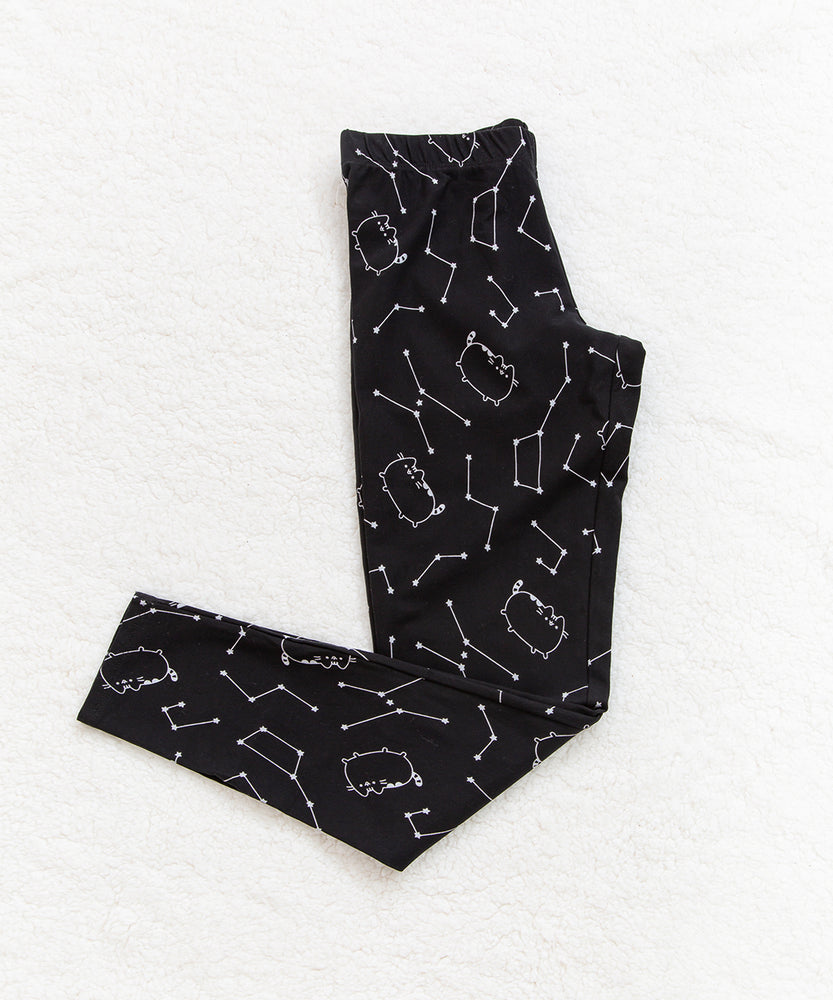 The Pusheen Celestial Leggings partially folded in half, on top of a white fuzzy blanket.