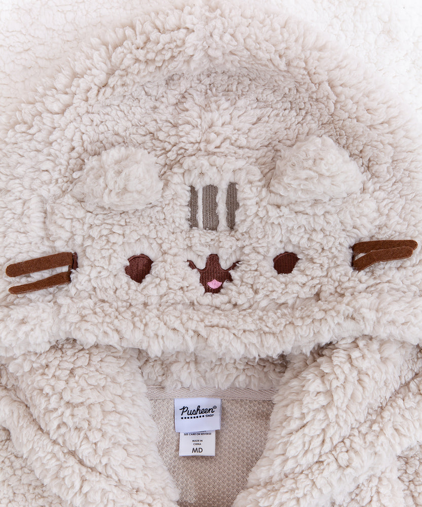 Close up of Pusheen's face on the hood. Pusheen's face and forehead stripes are embroidered into the hood and the whiskers are strips of brown felt. Pusheen's ears are made of the same fuzzy fabric as the rest of the hoodie. The interior of the hoodie is a light mech.