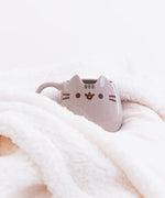 The Pusheen Character Mug tucked cozily among the folds of a fluffy white blanket.