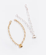Gold and Silver charm bracelets next to one another, with the gold chain curved like a circle and the silver chain pointed out in a 'v' shape. Both chains use a lobster claw clasp attached to an oval shape.