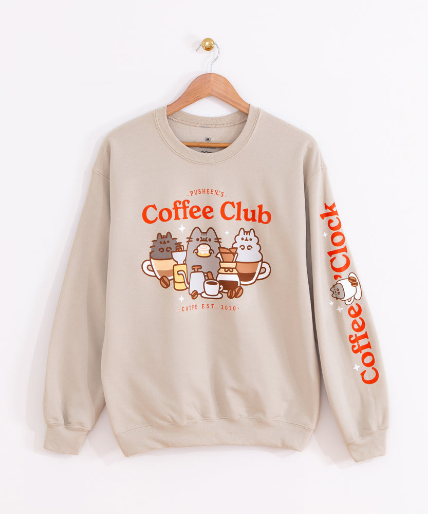 Front view of the Coffee Club Unisex Sweatshirt. The sand/tan sweatshirt hangs on a brown wood hanger to show all collar, sleeve, and hem details. 