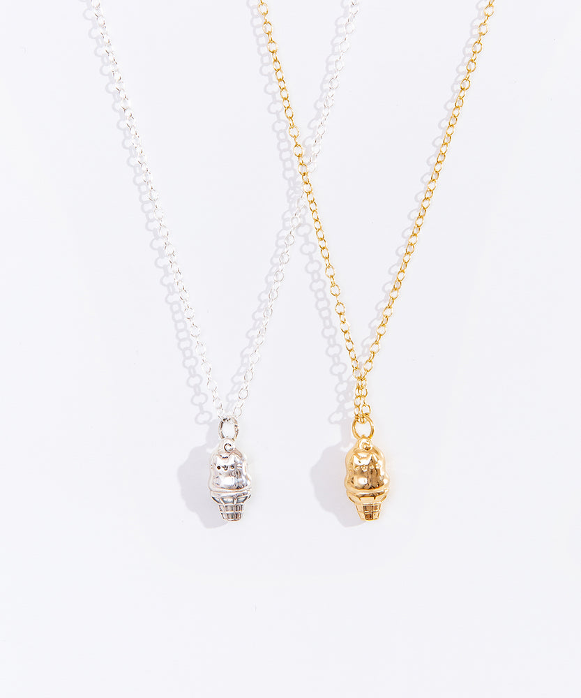 Front view of both Sterling Silver and Gold Vermeil finishes of the Pusheen Dipped Cone Charm Necklace. Hanging on the left is the sterling silver finish of the charm necklace and on the right is a gold vermeil finish. The necklace shows Pusheen the Cat as a dipped ice cream cone. 