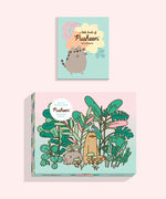 Front view of the box of the Pusheen Double-Sided 500-piece Puzzle. The plant-themed puzzle comes with a little book of Pusheen stickers. On the front of the puzzle box, there is a graphic of Pusheen, Sloth, and Bo the Parakeet surrounded by green and pink plants and foliage. A sticker on the front of the box says this puzzle is “2-in1 Double-Sided Pusheen 500-Piece Puzzle.” 