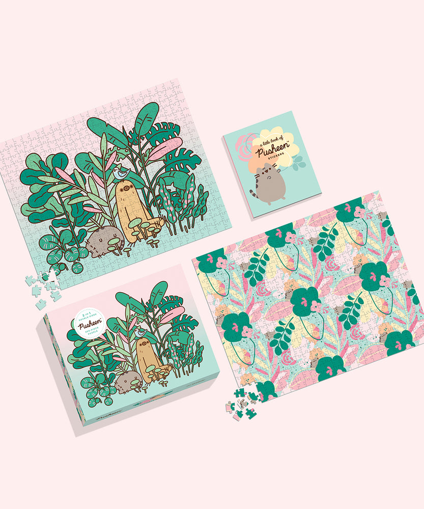 The Pusheen Double-Sided 500-Piece Puzzle box, sticker book, and both sides of the puzzle lie on a light pink surface. All elements feature graphic of Pusheen surrounded by plants and pink, yelllow, orange, and light blue details.  
