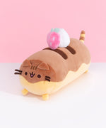 Front and side view of Pusheen Éclair Plush. Pusheen takes the form of a chocolate éclair treat. Her two-toned brown and yellow cylinder body is topped with a delicious pink strawberry and whipped cream dollop plush.