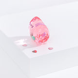 Side view of Pusheen Facets shows the width of the figurine scale. Figurine standing on a white surface surrounded by pink confetti hearts. Facets geometric reflection can be seen on white surface. 