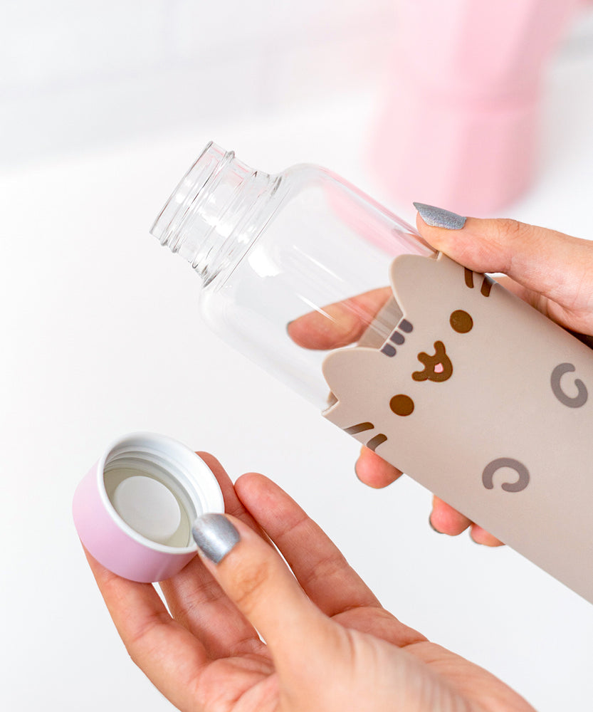 Close-up view of model holding glass water bottle. Model holds the lid of the water bottle to show the inside mechanism that seals the water bottle when closed.  