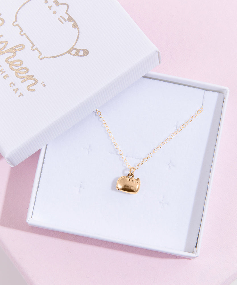 The gold charm necklace in a square white jewelry box. The jewelry lid features the Pusheen the Cat logo printed in silver.