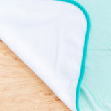 Close-up view of reverse side of blanket. The teal velour blanket is backed with a white velour. 