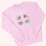 Front view of the Pusheen Holiday Gifts Unisex Sweatshirt lying on a light salmon background. The arms of the garment are folded in to show the cinched wrist and hem details of the sweatshirt.  