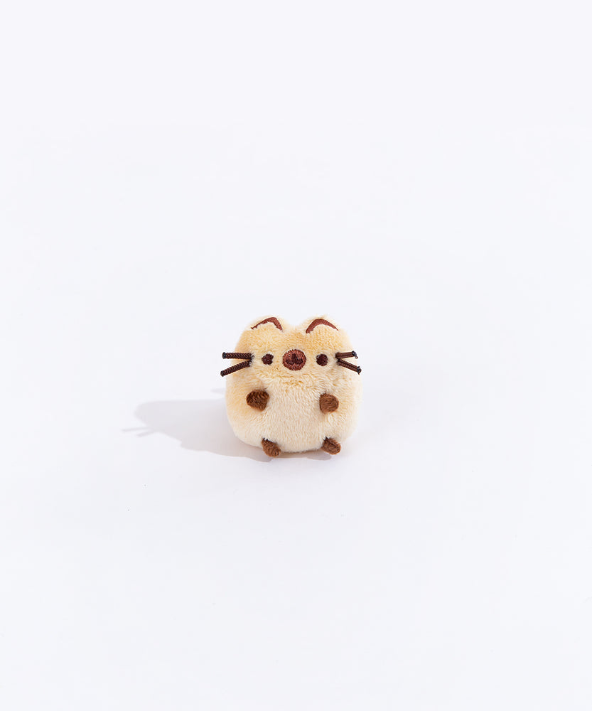 Full view of the mini Siamese cat plush from the collectors set. The cat is a light brown with dark brown paw stubs, a dark brown circle over their snout, and dark brown embroidered line on the top of their ears.
