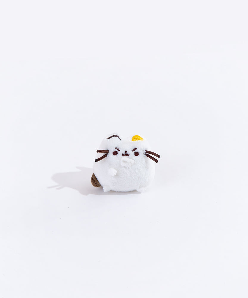 Full view of the mini annoyed white cat plush from the collectors set. The cat is all white, save for a brown embroidered dot on it’s left side, an embroidered dark brown line over its left ear and an embroidered yellow dot over their right ear. The plush has angry eye brows embroidered above their eyes, and their right paw is lifted up towards their mouth.