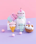 Group shot of five of the Pusheen Ice Cream characters sitting on white pedestals on a purple surface in front of a pink background. The Ice Cream characters included in this shot are Ice Pop Pusheen, Ice Cream Cup Pusheen, Strawberry Ice Cream Pusheen, Milkshake Pusheen, and Ice Cream Cake Pusheen. 